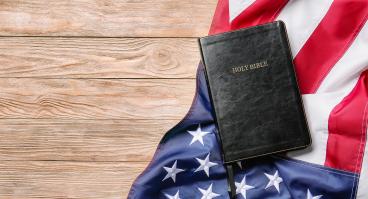 Holy Bible and American flag on wooden background